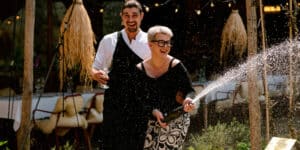 Webdesign Limburg | Two people celebrate outdoors as champagne sprays from a bottle they hold, smiling and laughing under string lights.